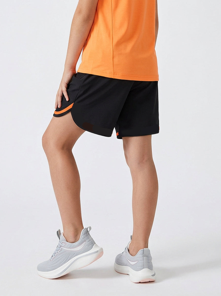 A child wearing black shorts with orange trim and gray athletic shoes on a white background