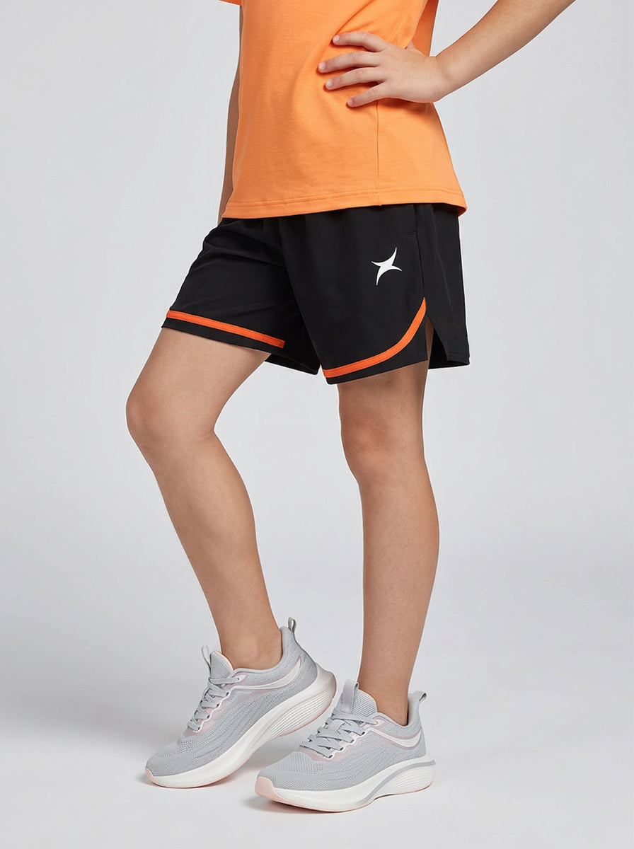 A child wearing black shorts with orange trim and an orange top on a light gray background