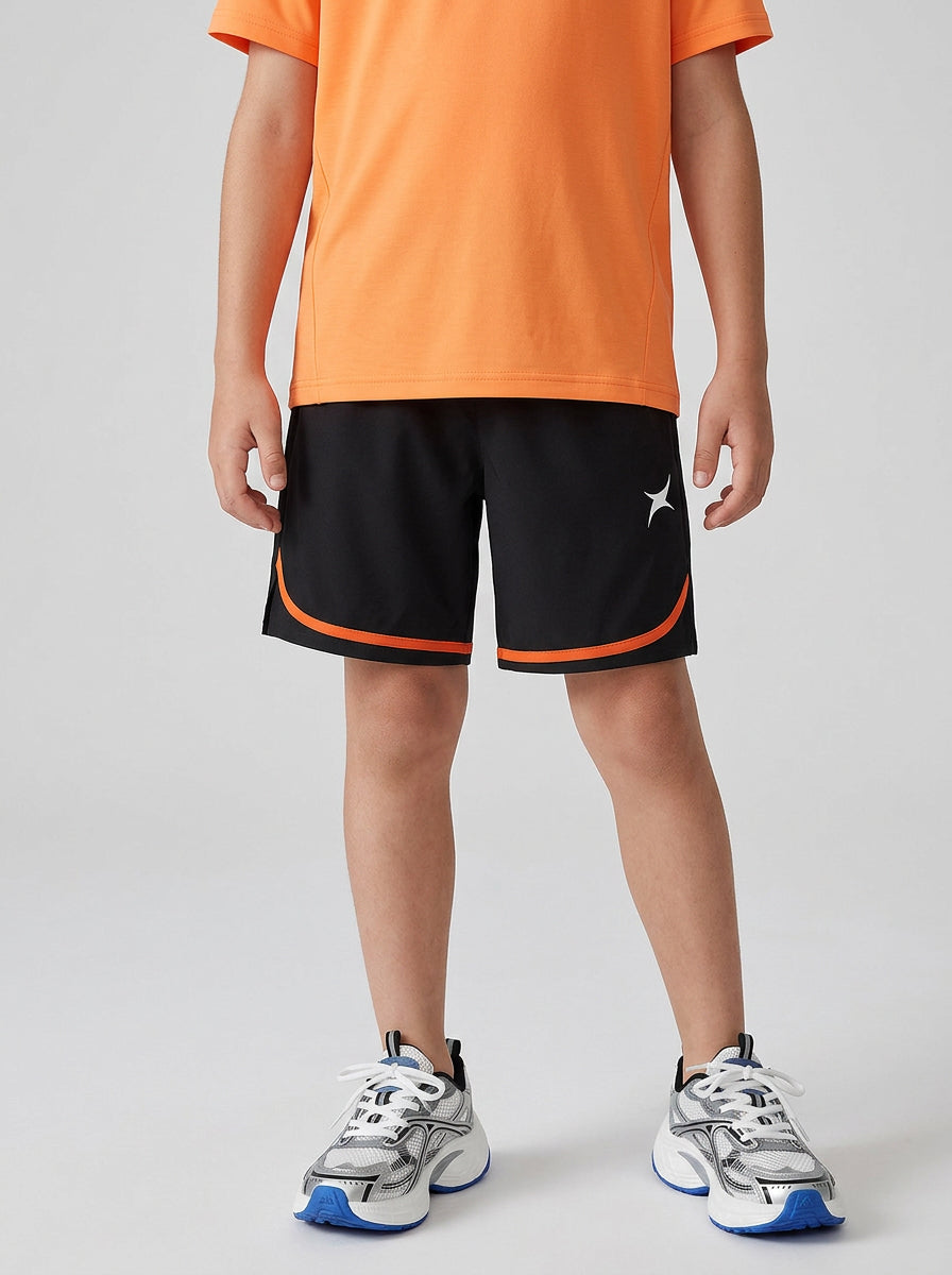 A boy wearing an orange T-shirt and black shorts with orange trim on a gray background