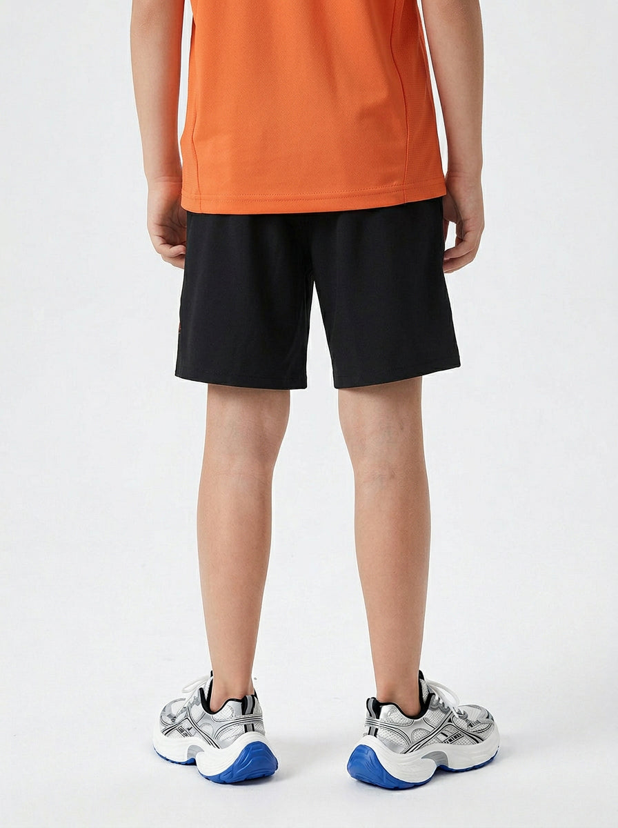 A boy wearing black shorts and orange T-shirt on a white background