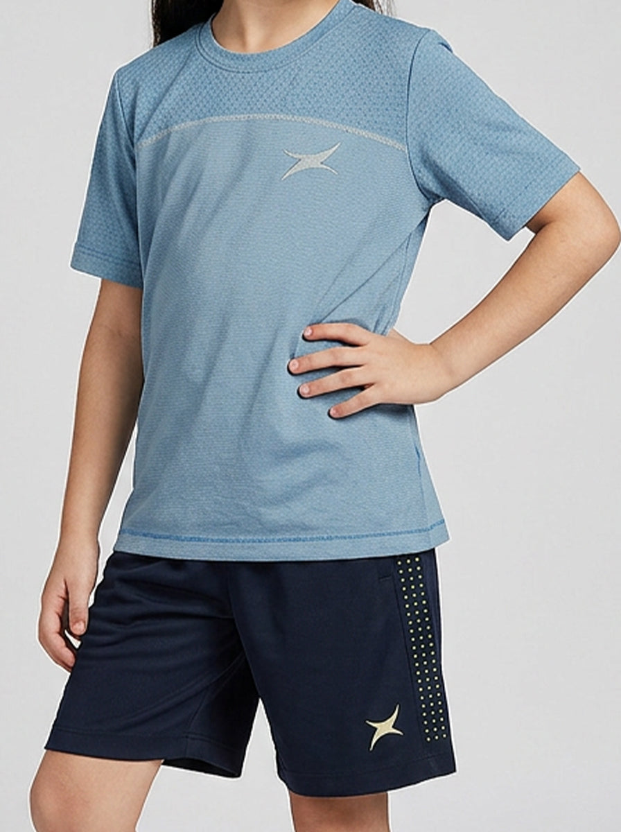 A girl wearing a blue sports t-shirt and navy shorts with a logo on a light gray background