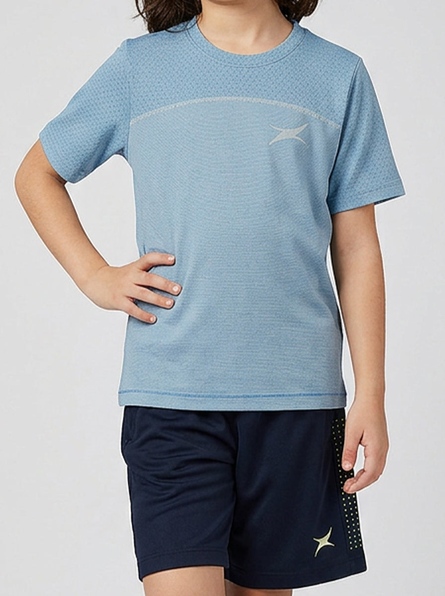 A girl wearing a blue sports shirt and navy shorts with a logo on a light gray background