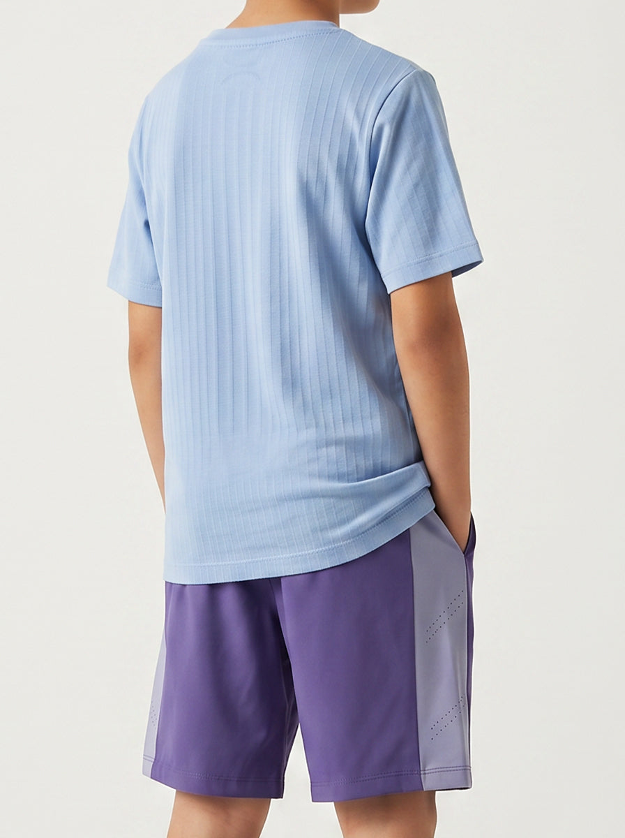 A child wearing a light blue sports t-shirt and purple shorts on a plain background