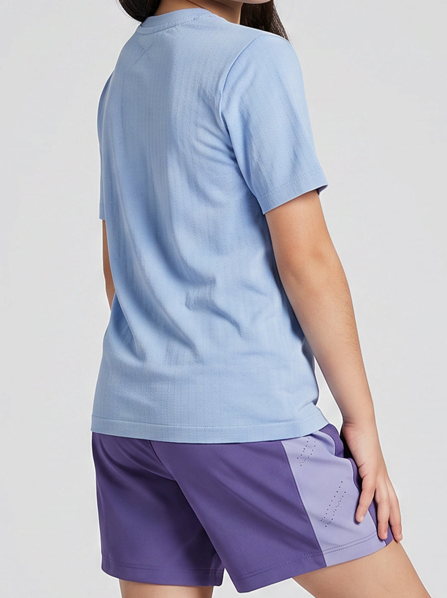 A girl wearing a light blue shirt and purple shorts on a plain background