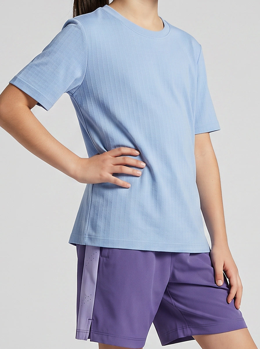 A girl wearing a light blue t-shirt and purple shorts on a gray background