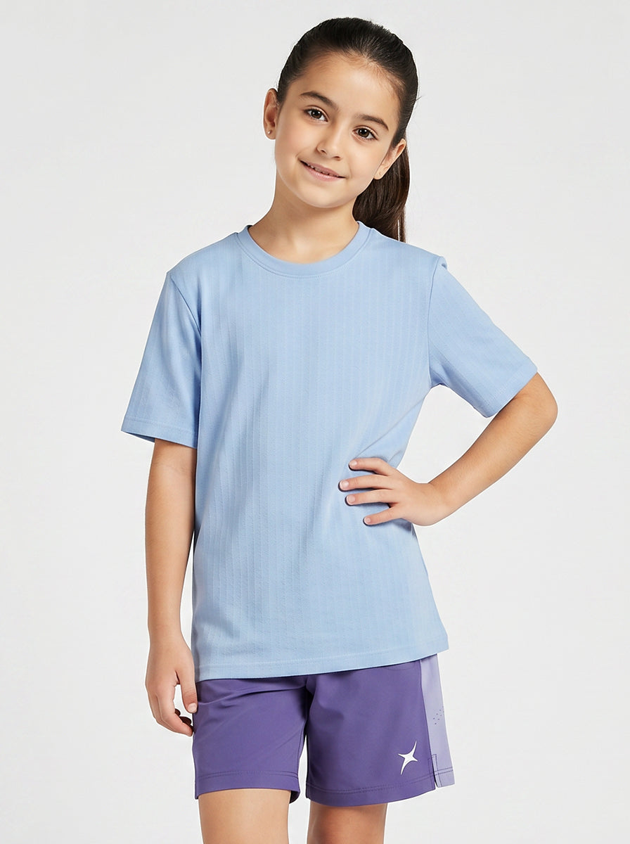 A girl wearing a light blue T- shirt and purple shorts on a white background