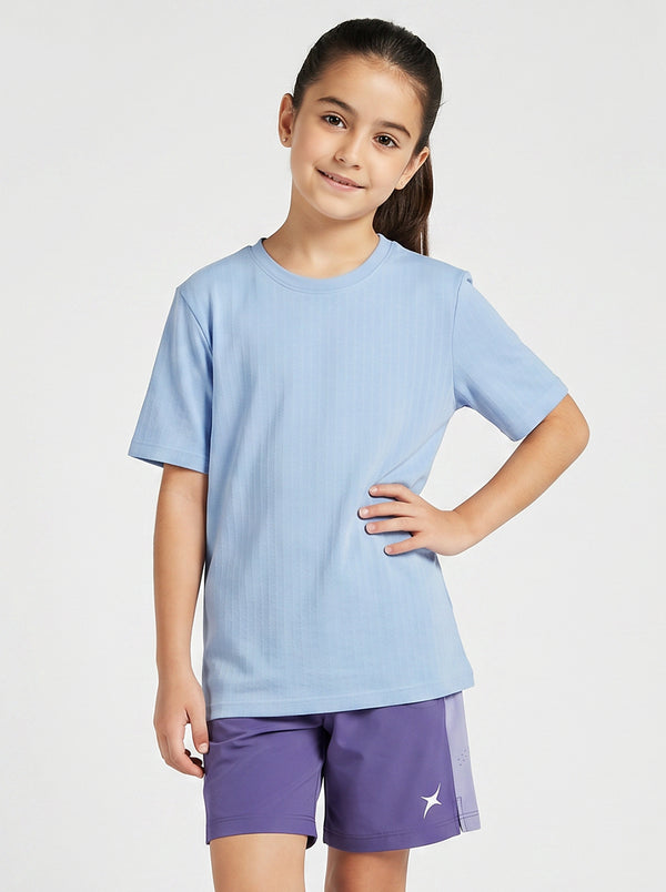A girl wearing a light blue T- shirt and purple shorts on a white background