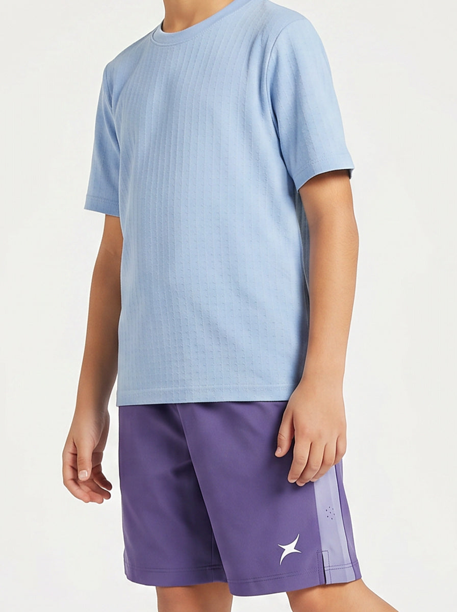 A child wearing a light blue sports t-shirt and purple shorts on a white background