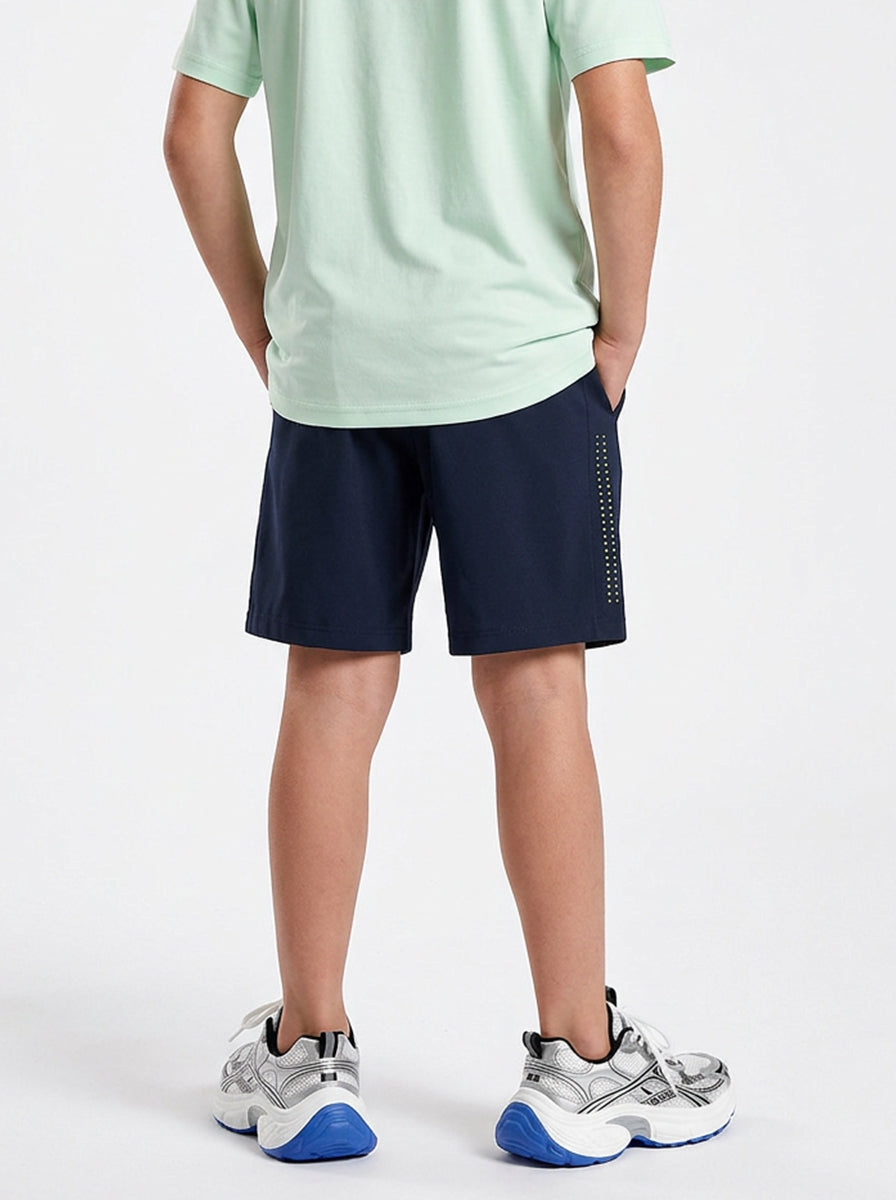A boy wearing a light green shirt and navy shorts on a white background