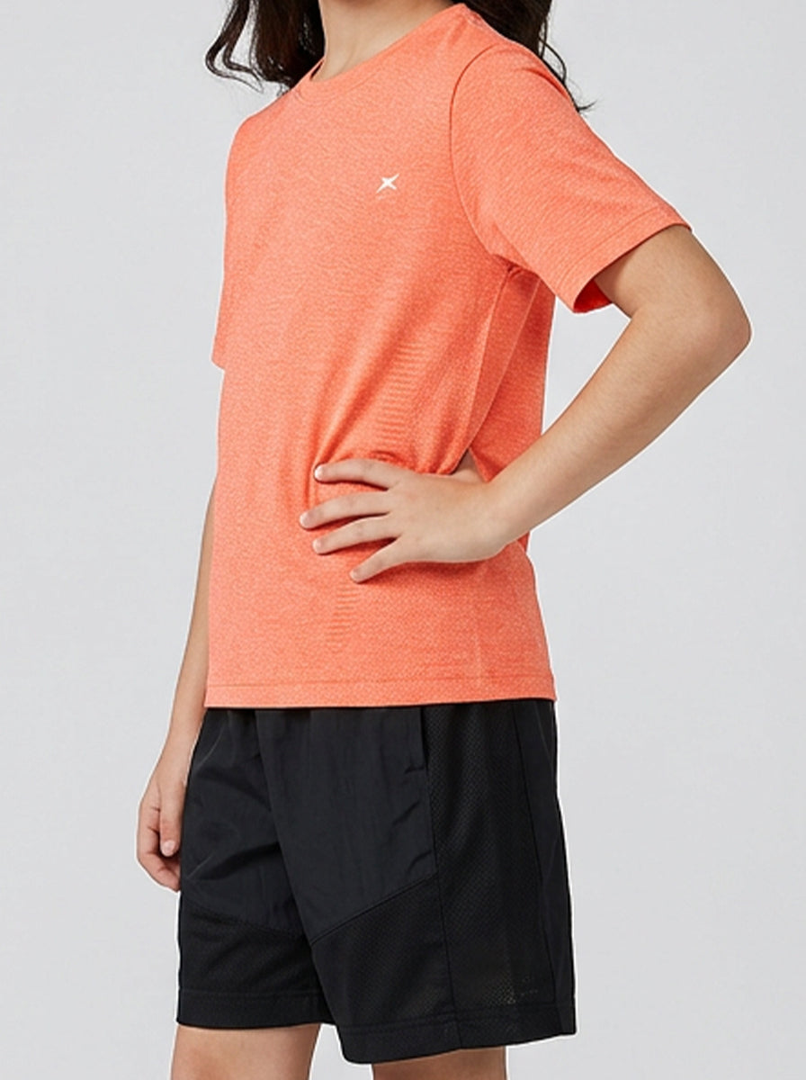 A girl wearing an orange t-shirt and black shorts on a light gray background