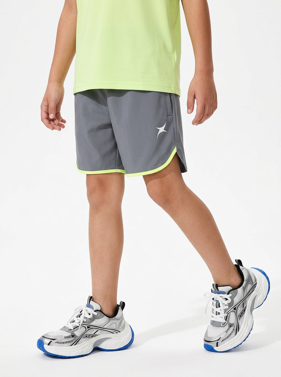 A boy wearing gray sports shorts with a neon yellow hem on a light gray background