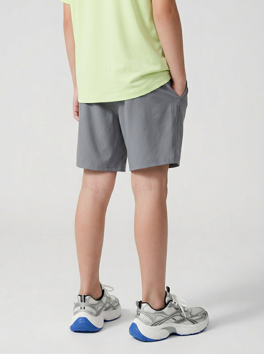A boy wearing gray shorts and a green T-shirt on a light gray background