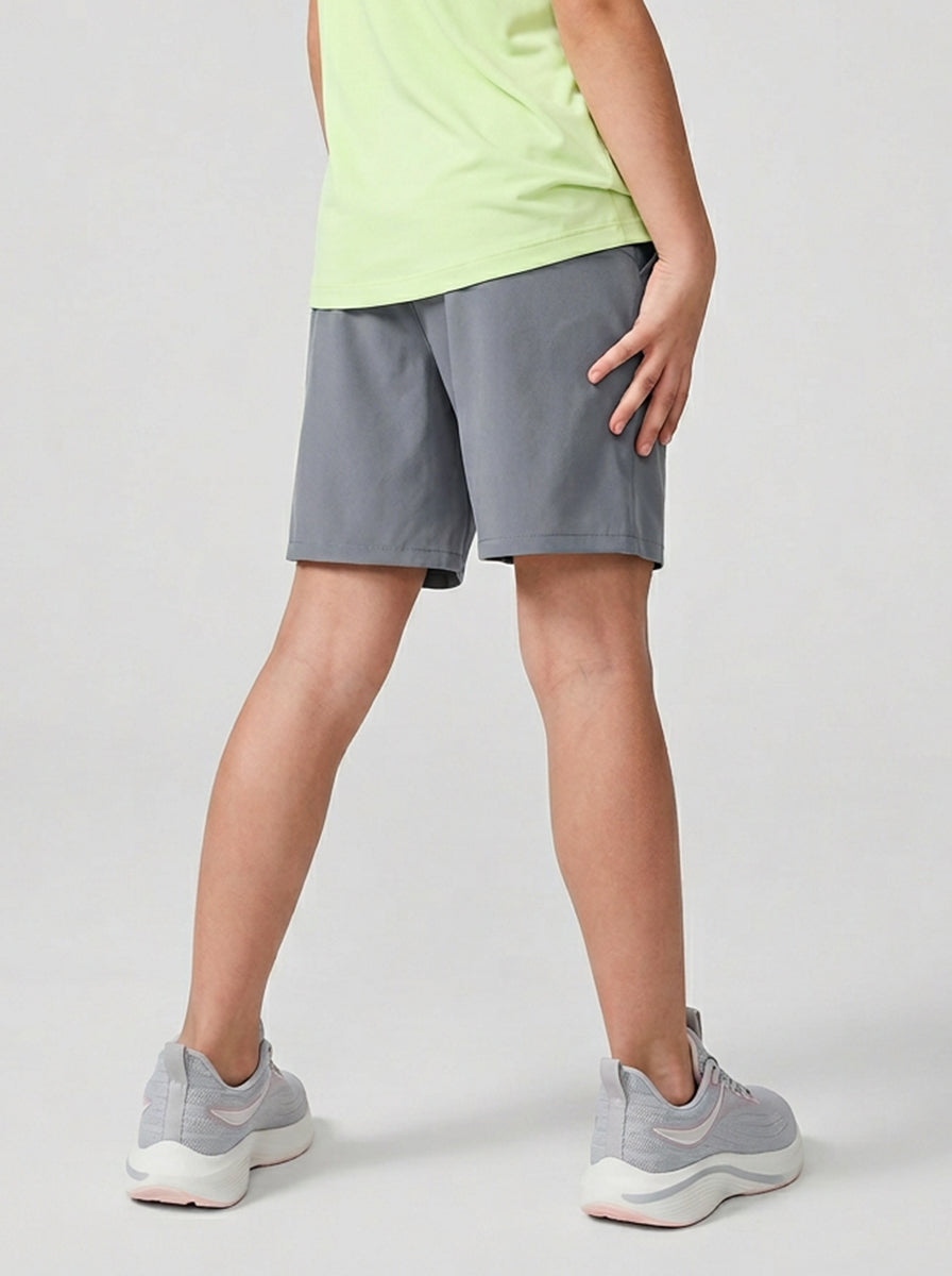 A child wearing gray shorts and light green top on a plain background