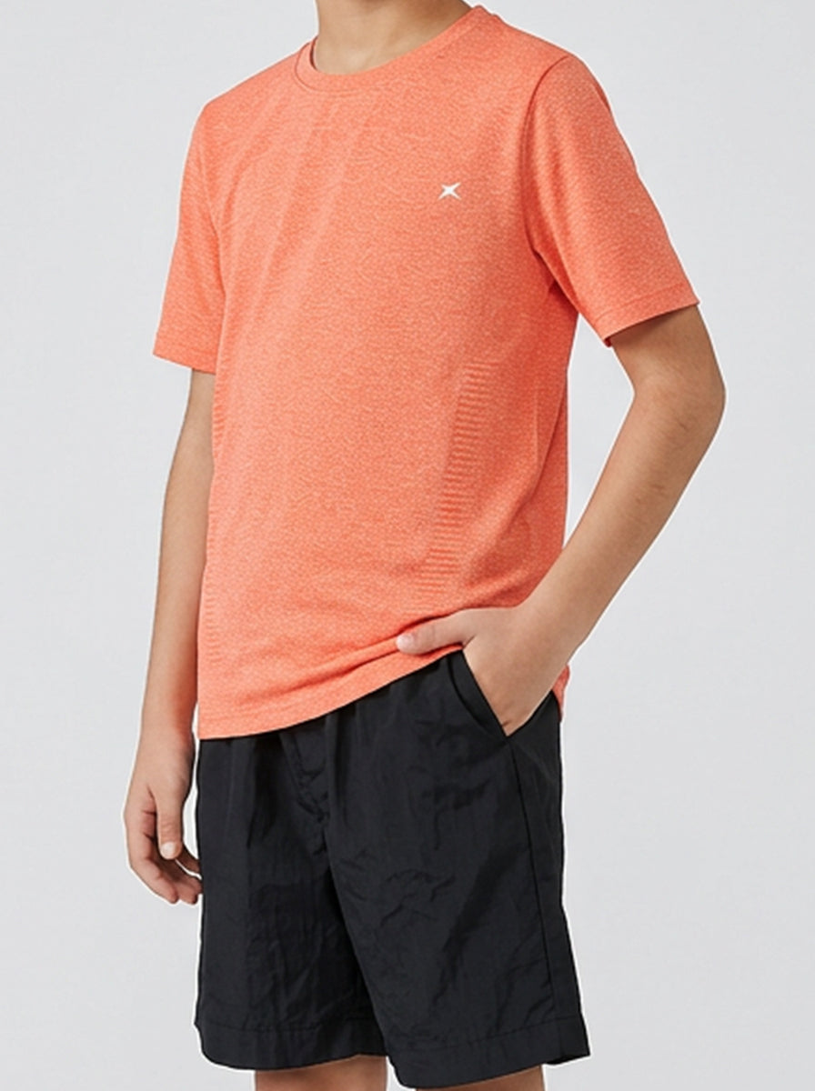 A boy wearing an orange t-shirt and black shorts on a light gray background