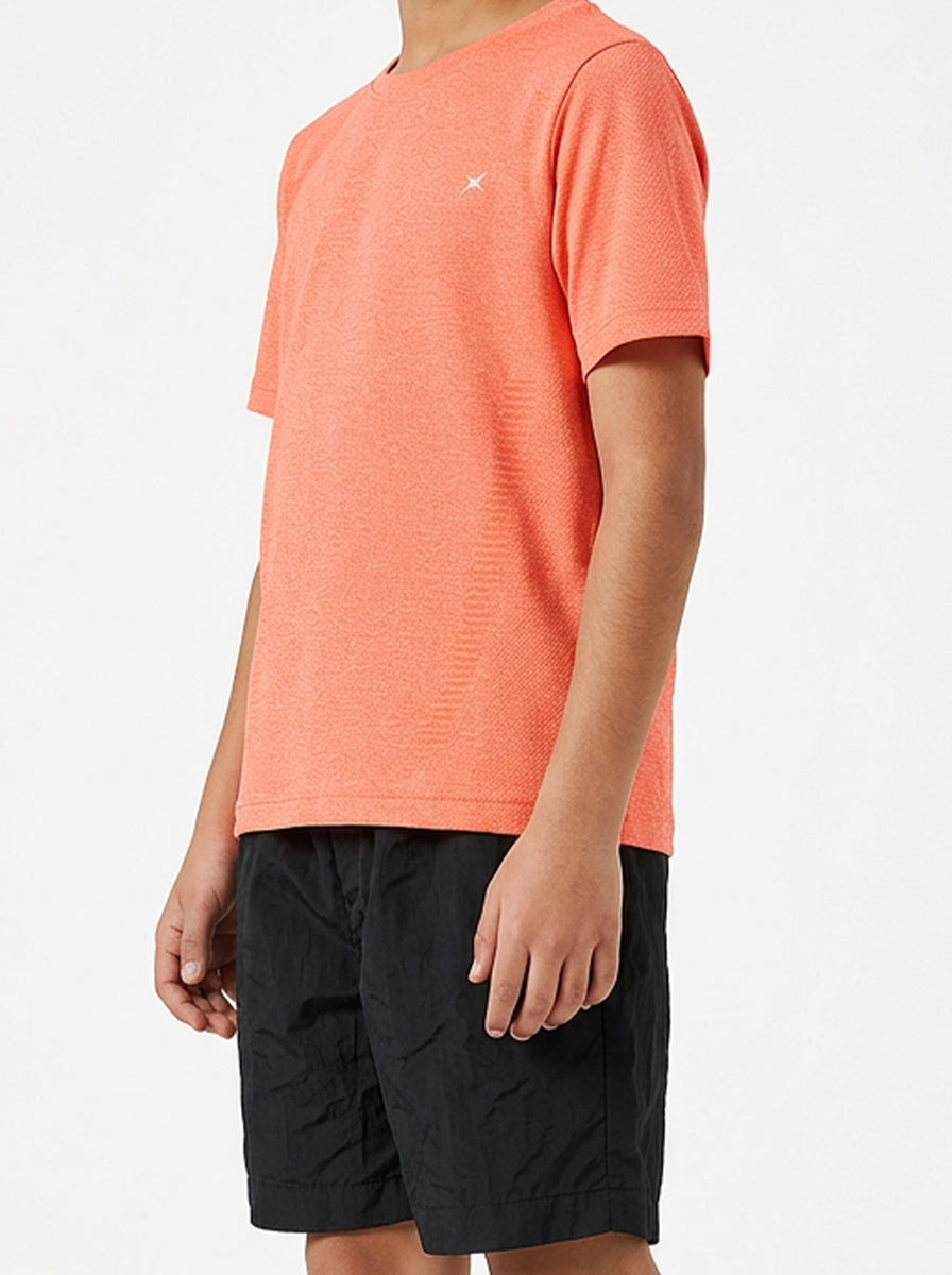 A boy wearing an orange t-shirt and black shorts on a light gray background