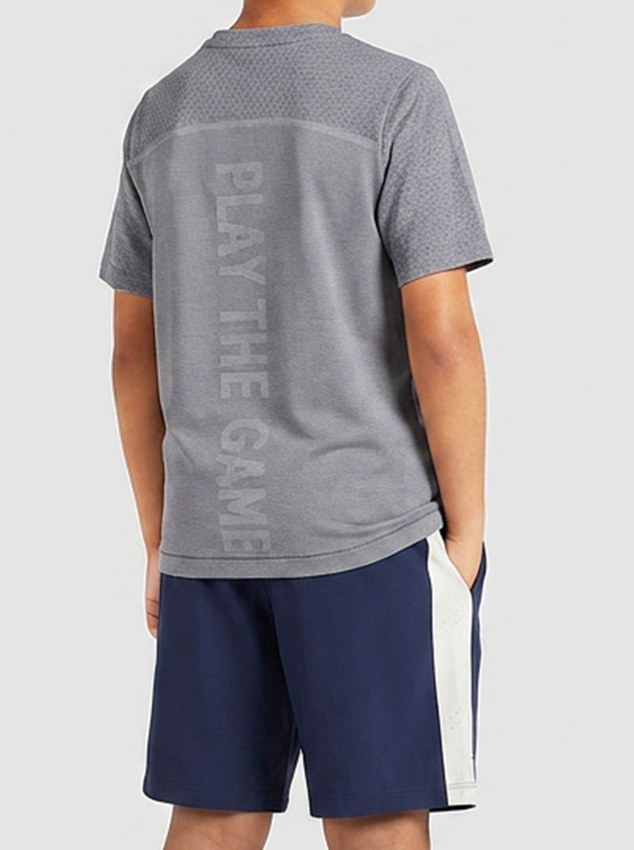 A boy wearing a gray t-shirt with 'Play The Game' text on the back and navy shorts.