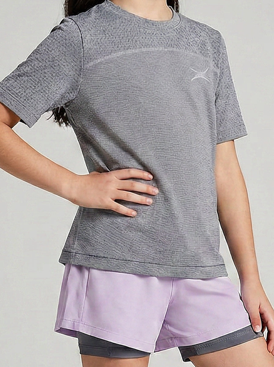 A girl wearing a gray sports shirt and purple shorts on a light gray background
