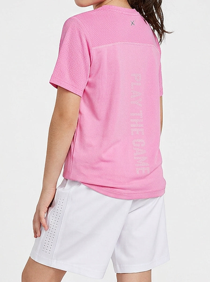 A girl wearing a pink shorts shirt with text on the back, standing against a white background