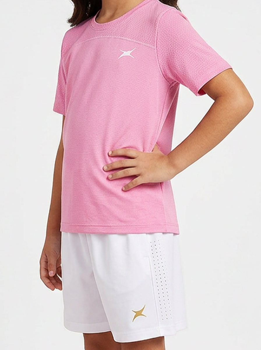 A girl wearing a pink sports t-shirt and white shorts with a brand logo on a light gray background