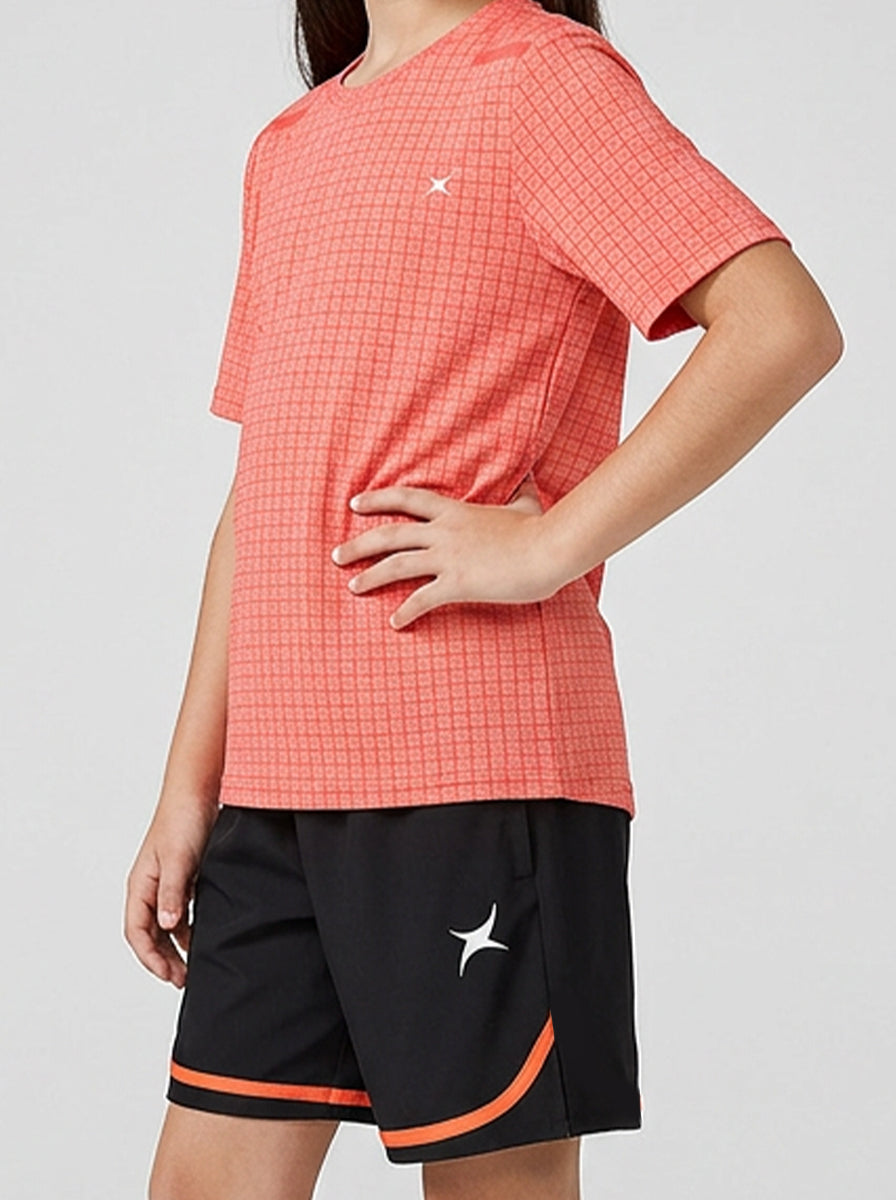 A girl wearing an orange sports checkered t-shirt and black shorts with orange trim on a light gray background