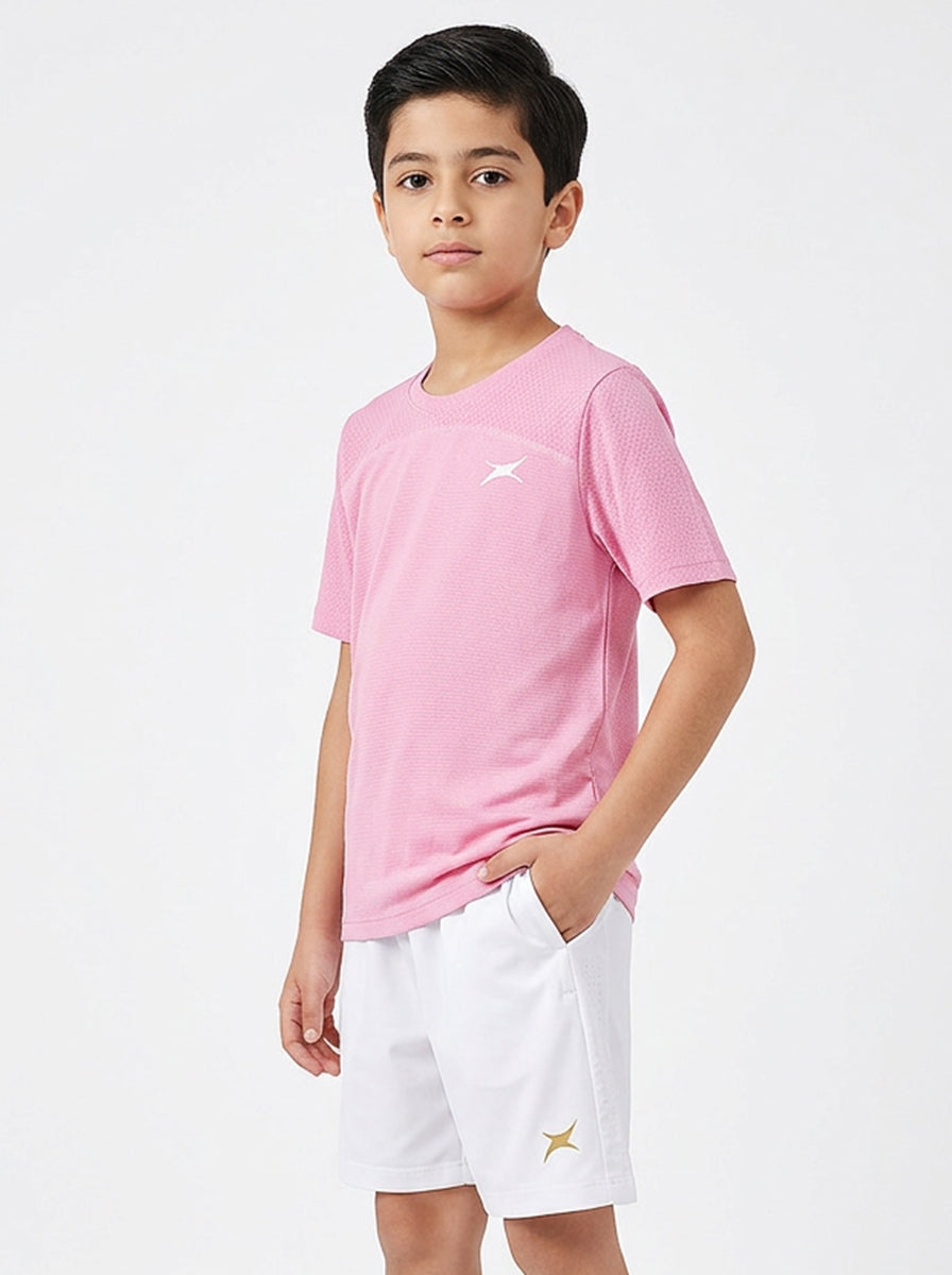 A boy wearing a pink sports t-shirt and white shorts on a light gray background